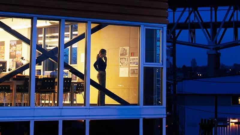 A woman looking pensively out a window of a modern building at night