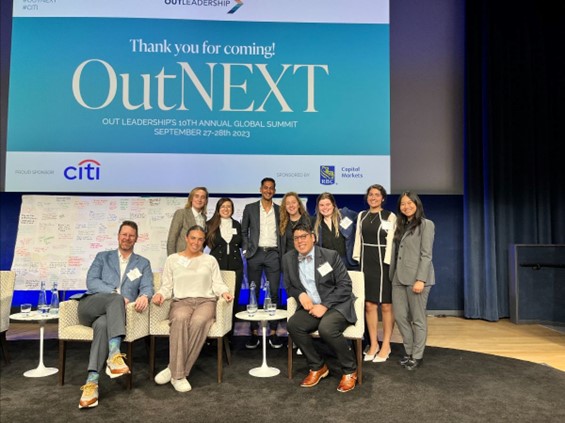 Photo of Connor Krone with fellow OutNEXT attendees at the 2023 OutNEXT Global Summit posing together in front of a large screen with text: Thank you for coming! OutNEXT. Out Leaderships 10th Annual Global Summit September 27-28, 2023. Sponsors Citi and RBC Capital Markets